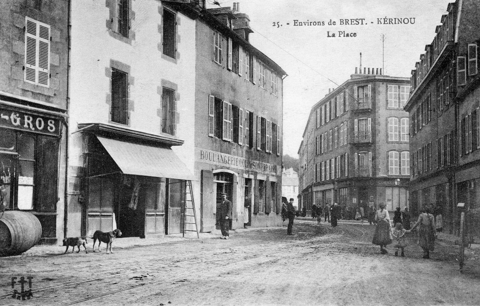 Carte postale ancienne en noir et blanc : la place de Kérinou, des maisons de deux étages, une boulangerie, des passants et deux chiens